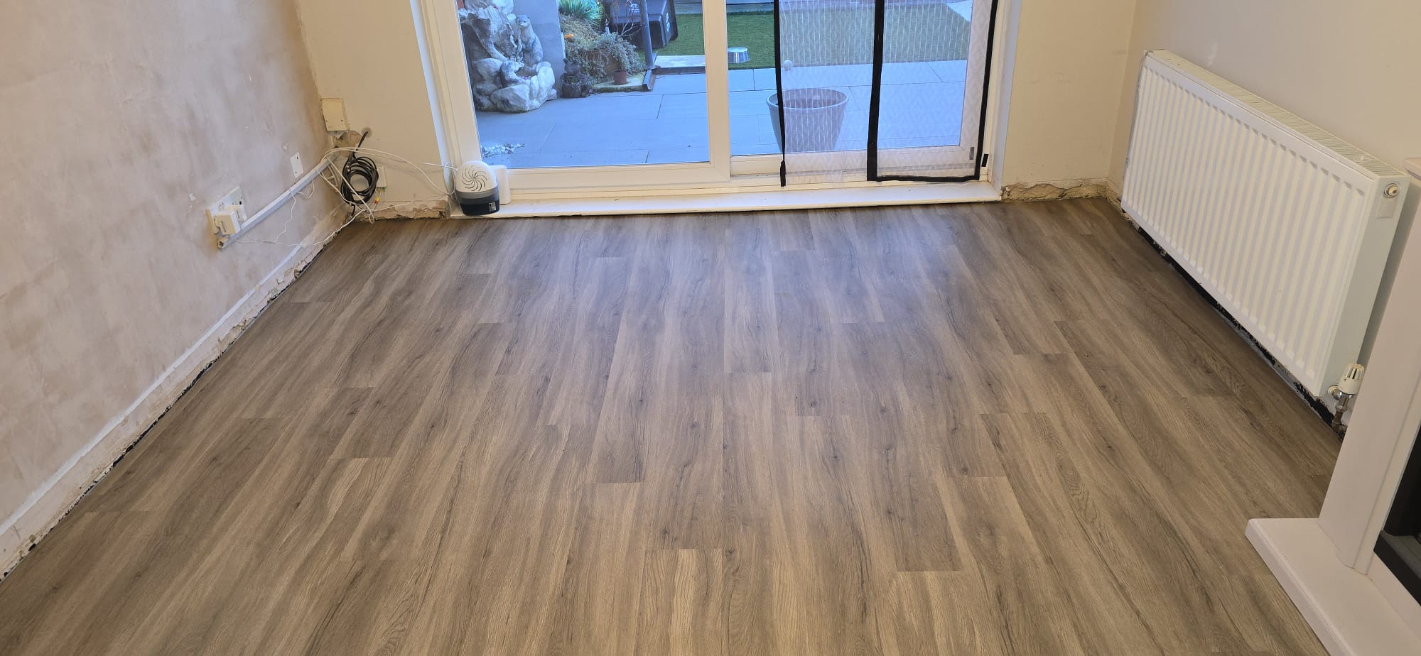 Grey oak plank flooring fitted in a lounge leading to patio doors in Northampton